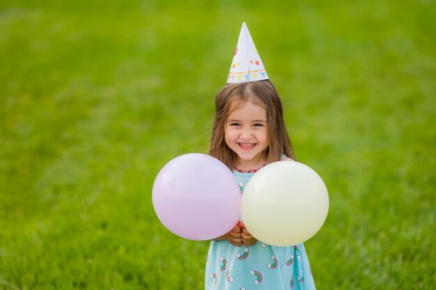 Hermosa niña en vestido azul y sombrero con globos en el parque feliz cumpleaños