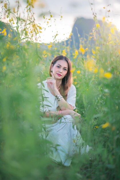 Una hermosa niña con un vestido blanco fotografiada en medio de un campo amarillo con flores al atardecer.