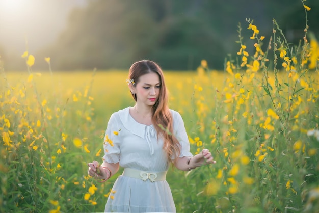 Una hermosa niña con un vestido blanco fotografiada en medio de un campo amarillo con flores al atardecer.