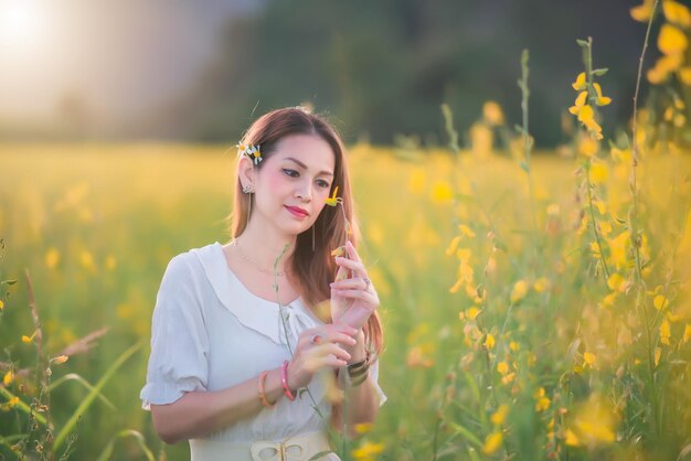 Una hermosa niña con un vestido blanco fotografiada en medio de un campo amarillo con flores al atardecer.