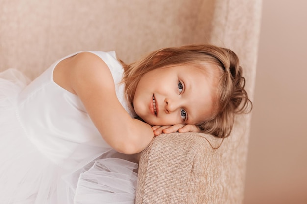 Hermosa niña en vestido blanco posa para la cámara en silla