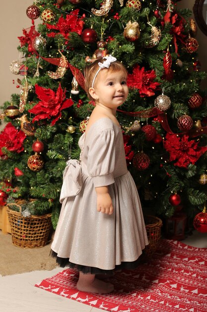 hermosa niña con un vestido festivo se encuentra junto al árbol de navidad