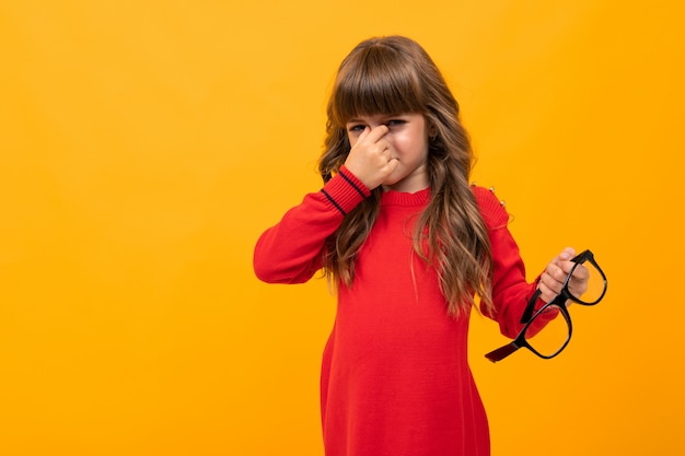 Hermosa niña en vestido juega con gafas aisladas en amarillo y naranja