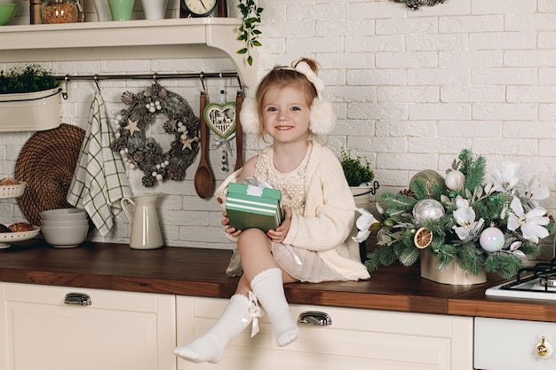 Hermosa niña en un vestido con un regalo en la mano sentada en la mesa de la cocina