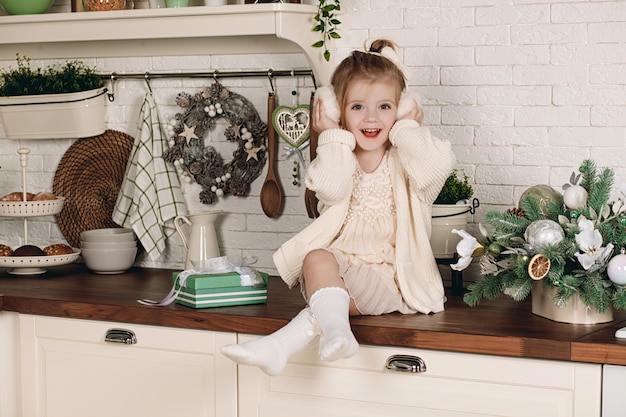 Hermosa niña en un vestido con un regalo sentado en la mesa de la cocina. Vacaciones de invierno