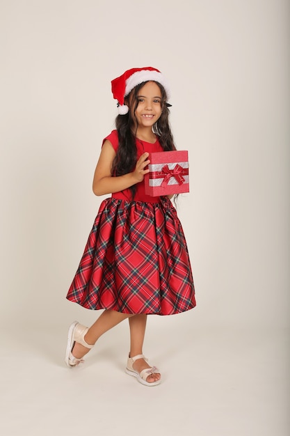 Una hermosa niña con un vestido rojo y un sombrero de Santa Claus tiene una caja de regalo en sus manos