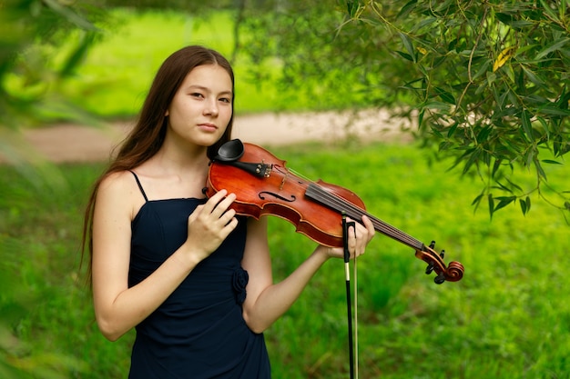 Una hermosa niña con violinistas largos se encuentra en el parque en verano. Foto de alta calidad