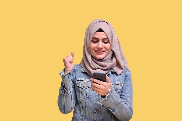 Hermosa niña vistiendo hijab con jeans feliz y usando teléfono modelo paquistaní indio