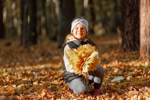 Hermosa niña vistiendo jugando con hojas secas tirándolas al aire