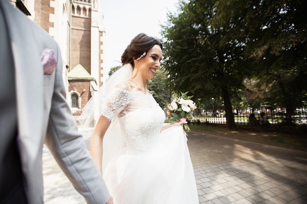 Hermosa novia camina con su novio cerca de la antigua iglesia cristiana