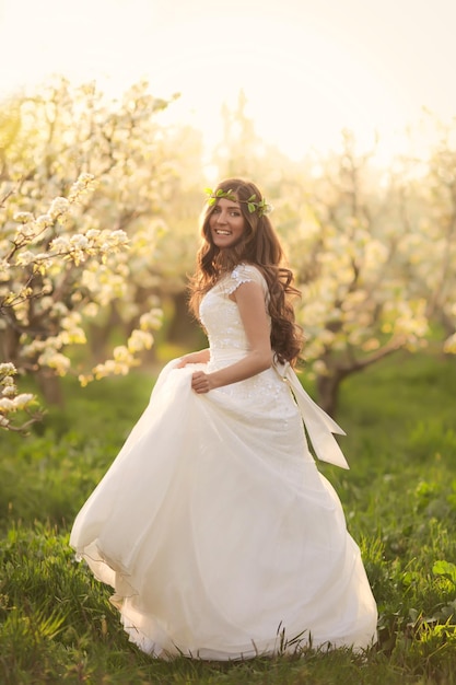 Hermosa novia de cuento de hadas en vestido de novia con cabello largo caminando en jardines con flor