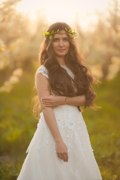 Hermosa novia de cuento de hadas en vestido de novia con cabello largo caminando en jardines con flor