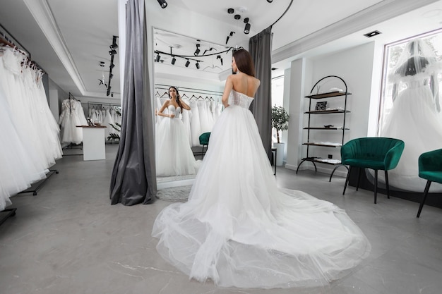 La hermosa novia delgada se prueba un vestido de novia en un salón de belleza frente a un espejo.