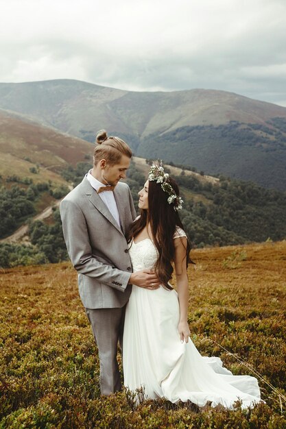 Hermosa novia y elegante novio posando abrazando boda boho pareja ceremonia de lujo en las montañas con una vista increíble