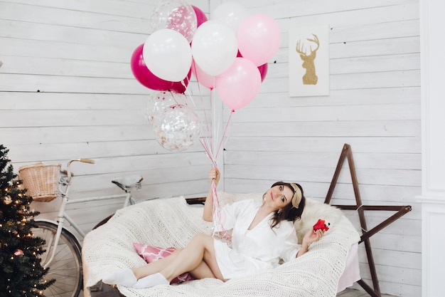 Hermosa novia feliz con globos de aire rosa en un sillón acogedor