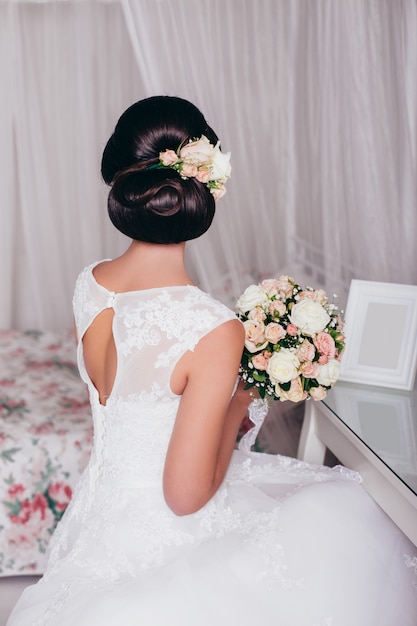 Hermosa novia con flores, vestido y peinado de boda elegante