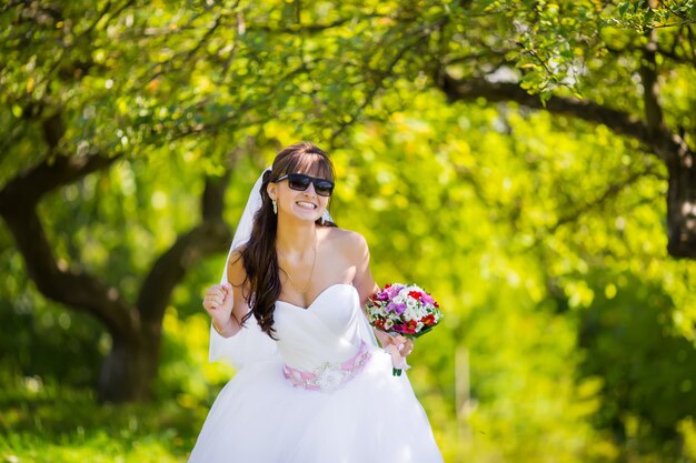 Hermosa novia en gafas de sol posando en el parque