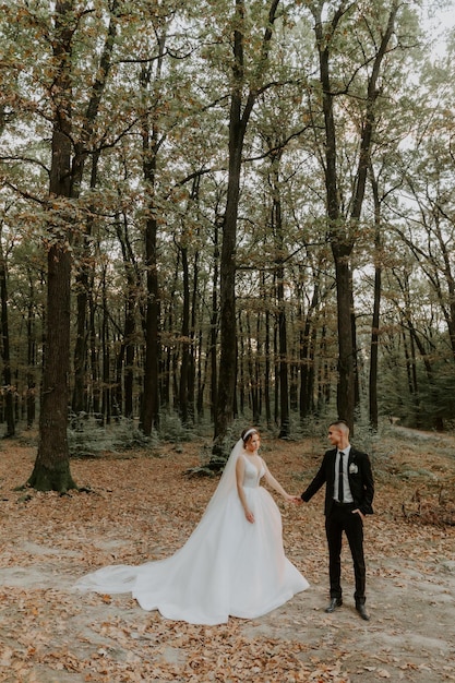 Hermosa novia con un largo vestido blanco. Novio guapo con traje negro. Pareja en un parque de verano