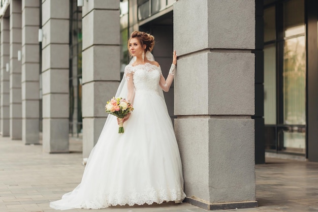 Hermosa novia con lujoso vestido blanco en una calle de la ciudad