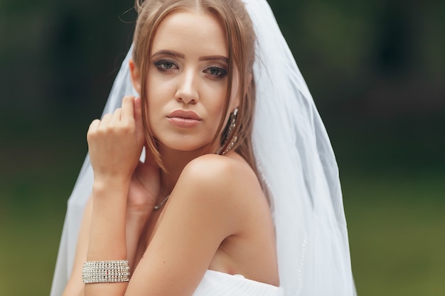 Hermosa novia en un magnífico vestido de novia posando entre vegetación en la calle. Concepto de novia para vestidos publicitarios.