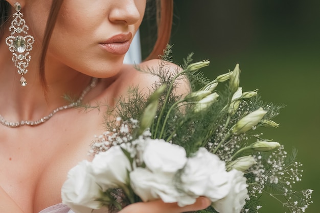 Hermosa novia en un magnífico vestido de novia posando entre vegetación en la calle