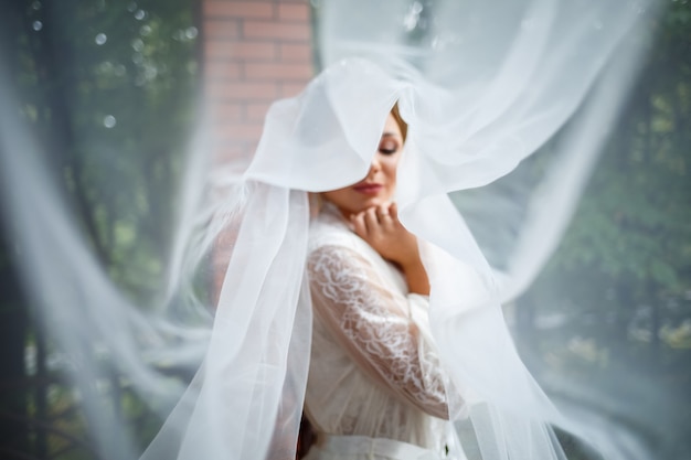 Hermosa novia en una mañana de bodas en albornoz y velo