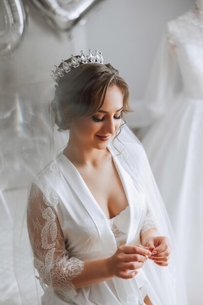 Foto una hermosa novia morena con una tiara en el cabello se está preparando para la boda en una hermosa túnica en estilo boudoir foto de retrato de boda en primer plano