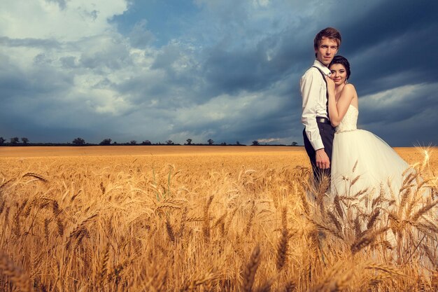 Hermosa novia y novio en campo de trigo con cielo azul de fondo. Fotografía de boda