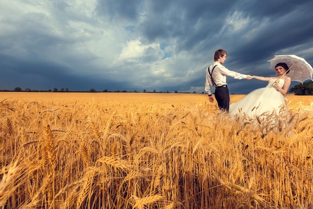 Hermosa novia y novio en campo de trigo con cielo azul en el fondo. Fotografía de boda