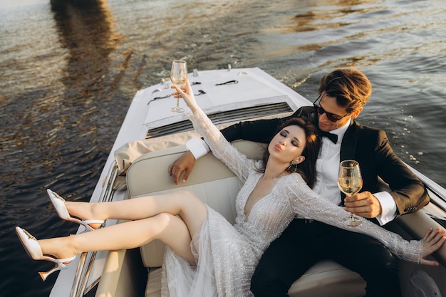 Hermosa novia y novio montan un yate beben vino y disfrutan el momento Día de la boda