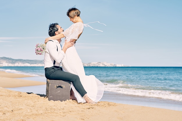 Hermosa novia y el novio en la playa mirándose con mucho amor y alegría