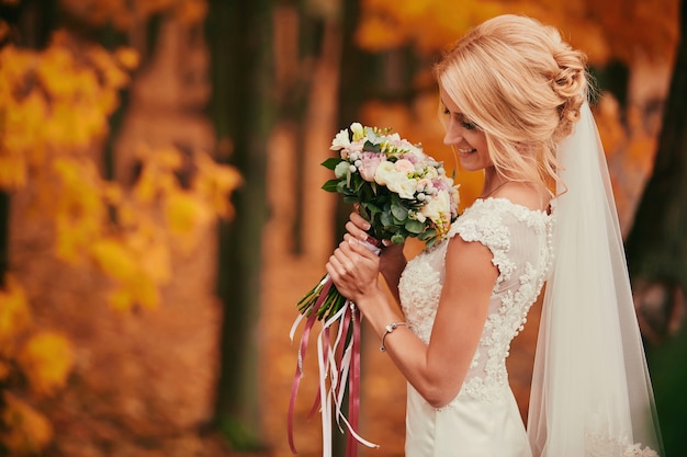 Hermosa novia oliendo ramo de novia en el parque otoño