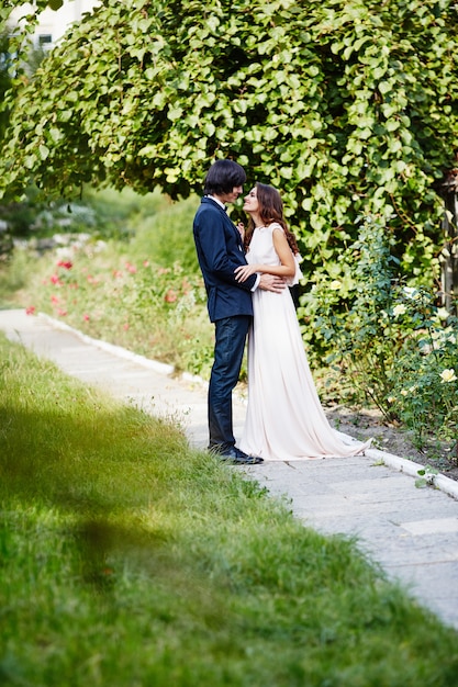 Hermosa novia con el pelo largo y rizado y el novio de pie cerca uno del otro en el fondo de hojas verdes, foto de boda, retrato.