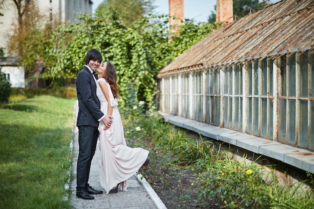 Hermosa novia con el pelo largo y rizado y el novio de pie cerca uno del otro en hojas verdes, foto de boda, hermosa pareja.