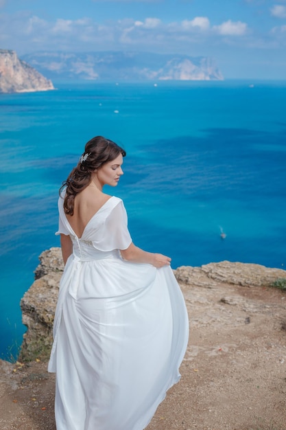 Una hermosa novia de pie en la costa La novia en las montañas Boda Romántica novia hermosa en vestido blanco posando en el mar de fondo