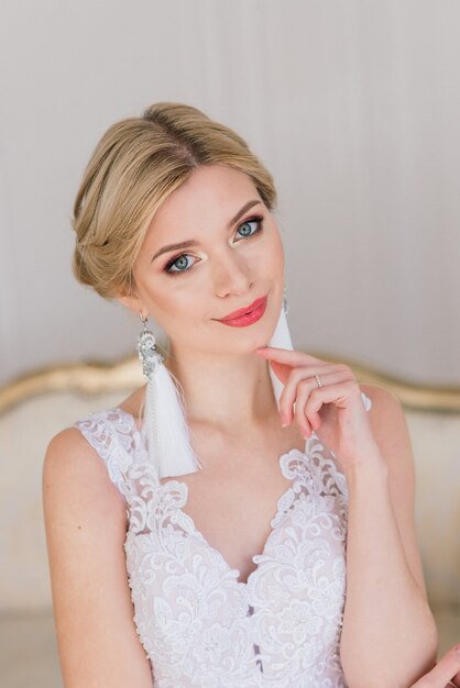 Hermosa novia posando en vestido de novia en un sofá, espejo y estudio fotográfico blanco.