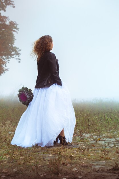 Hermosa novia con un ramo de flores en campo brumoso