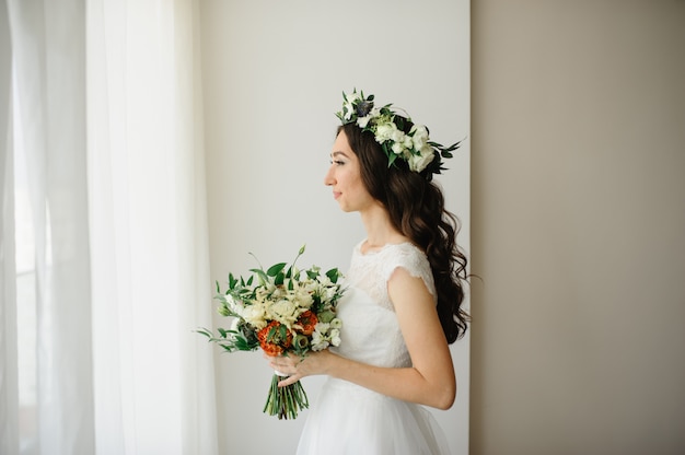 Hermosa novia con un ramo de flores y una corona de flores en la cabeza.