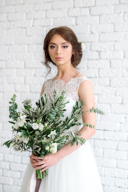 Hermosa novia con ramo de flores. morena en una pared de ladrillo blanco leonado