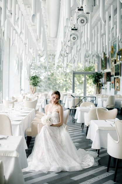 Hermosa novia con un ramo en la mano se sienta en un restaurante el día de la boda