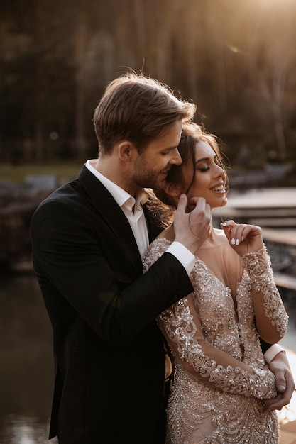 Hermosa novia con un ramo moderno abrazando a un elegante novio en el parque de verano.