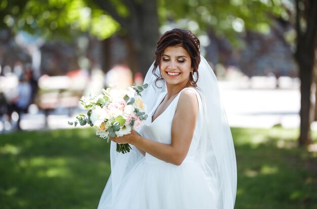 Hermosa novia con ramo de novia para caminar en el parque Novia joven en vestido blanco Día de la boda