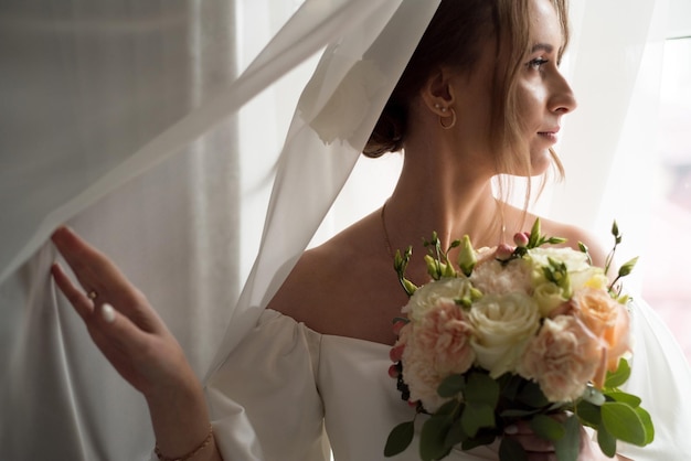 Hermosa novia con ramo de novia junto a la ventana