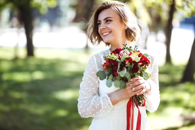 Hermosa novia con ramo de novia en el parque Mujer elegante con maquillaje profesional y peinado