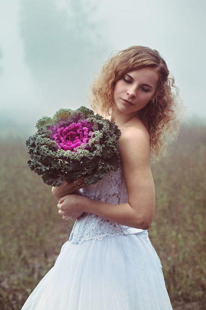 Hermosa novia con un ramo sobre un fondo de un campo brumoso