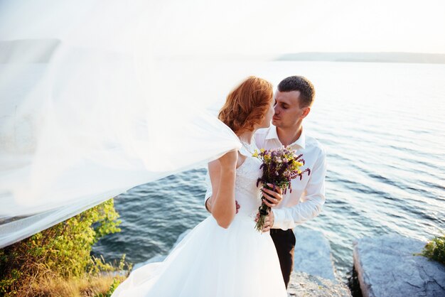 Hermosa novia rubia y novio con clase en las rocas, en medio del mar