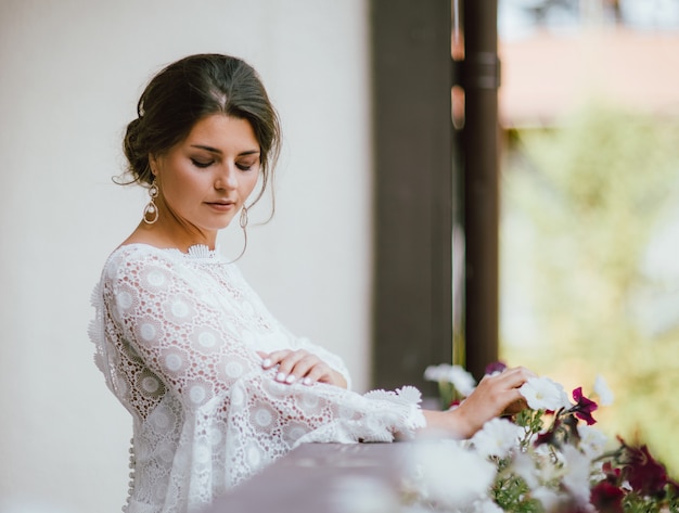 Hermosa novia sonriente morena joven en vestido de encaje blanco en el balcón