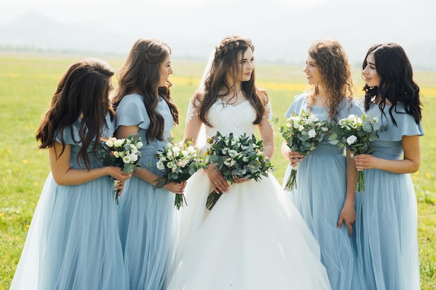 hermosa novia y sus doncellas de pie con flores en la naturaleza