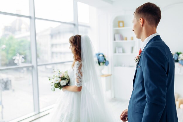 Hermosa novia vestida de blanco y el novio en traje, posando en blanco Studio interior, boda