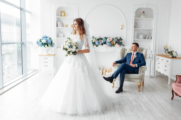 Hermosa novia vestida de blanco y el novio en traje, posando en blanco Studio interior, boda